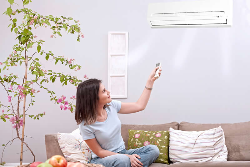 woman sitting on sofa controlling ductless ac with remote