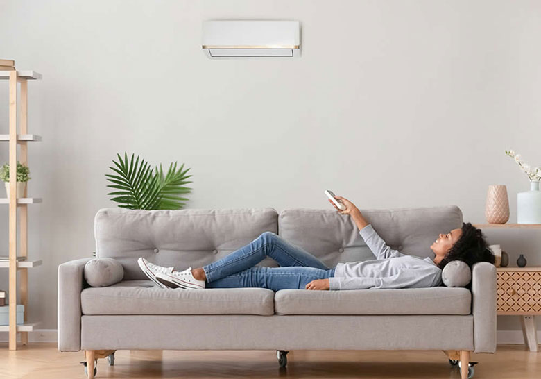 woman lying on sofa using remote to control ductless ac